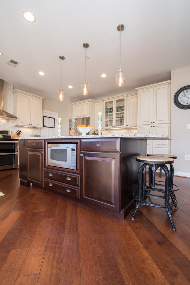 Large country u-shaped separate kitchen in DC Metro with raised-panel cabinets, white cabinets, granite benchtops, white splashback, subway tile splashback, stainless steel appliances, dark hardwood floors, with island, brown floor, grey benchtop and a farmhouse sink.
