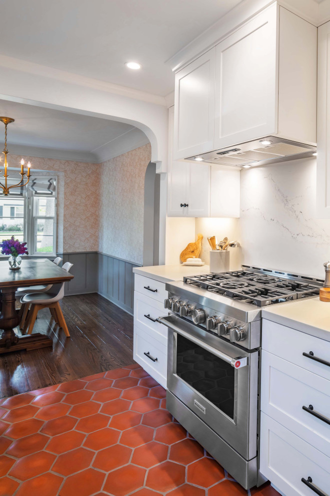 Foto på ett mellanstort medelhavsstil vit kök, med en rustik diskho, skåp i shakerstil, vita skåp, bänkskiva i kvarts, vitt stänkskydd, rostfria vitvaror, klinkergolv i terrakotta, en halv köksö och rött golv