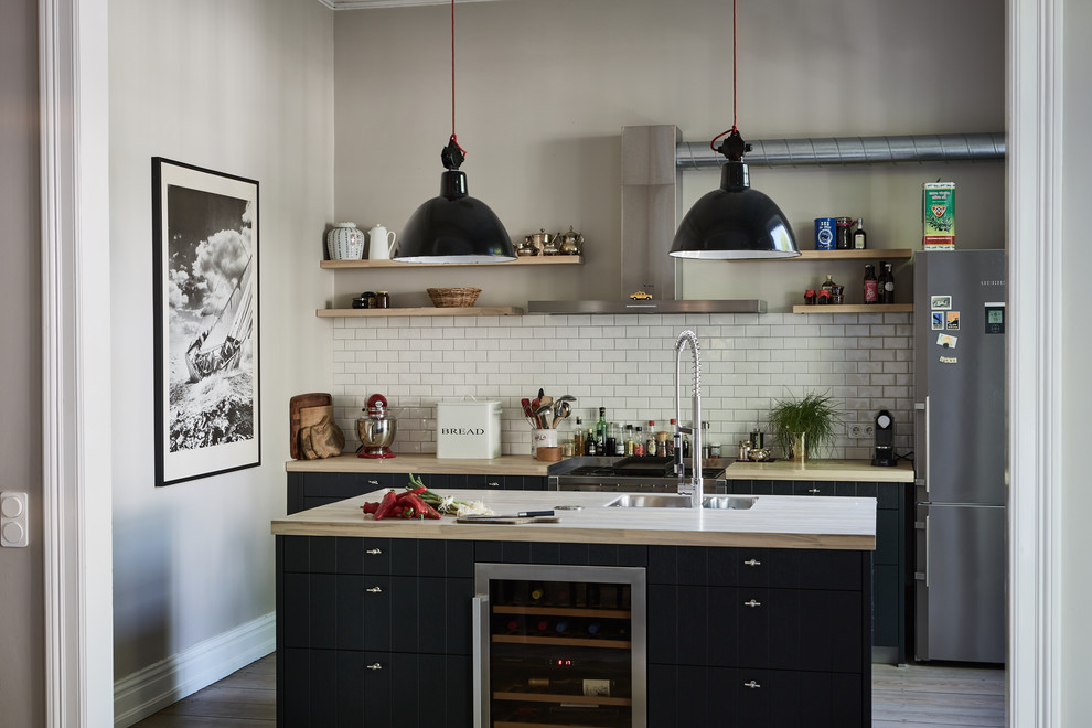 This is an example of a contemporary kitchen in Hamburg with a double-bowl sink, raised-panel cabinets, black cabinets, wood benchtops, white splashback, ceramic splashback, with island, grey floor and beige benchtop.