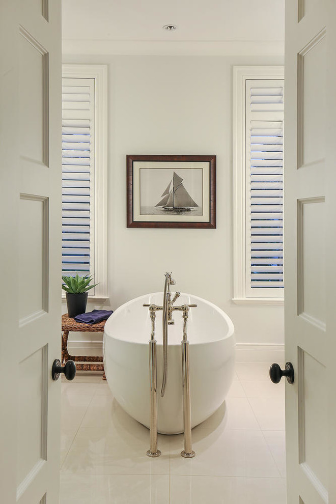 Design ideas for a large tropical master bathroom in Tampa with recessed-panel cabinets, white cabinets, a freestanding tub, a corner shower, a two-piece toilet, beige tile, ceramic tile, white walls, porcelain floors, an undermount sink and marble benchtops.