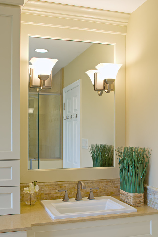 Design ideas for a mid-sized transitional master bathroom in New York with recessed-panel cabinets, white cabinets, solid surface benchtops, beige tile, a drop-in sink, a shower/bathtub combo, a one-piece toilet, beige walls and limestone floors.