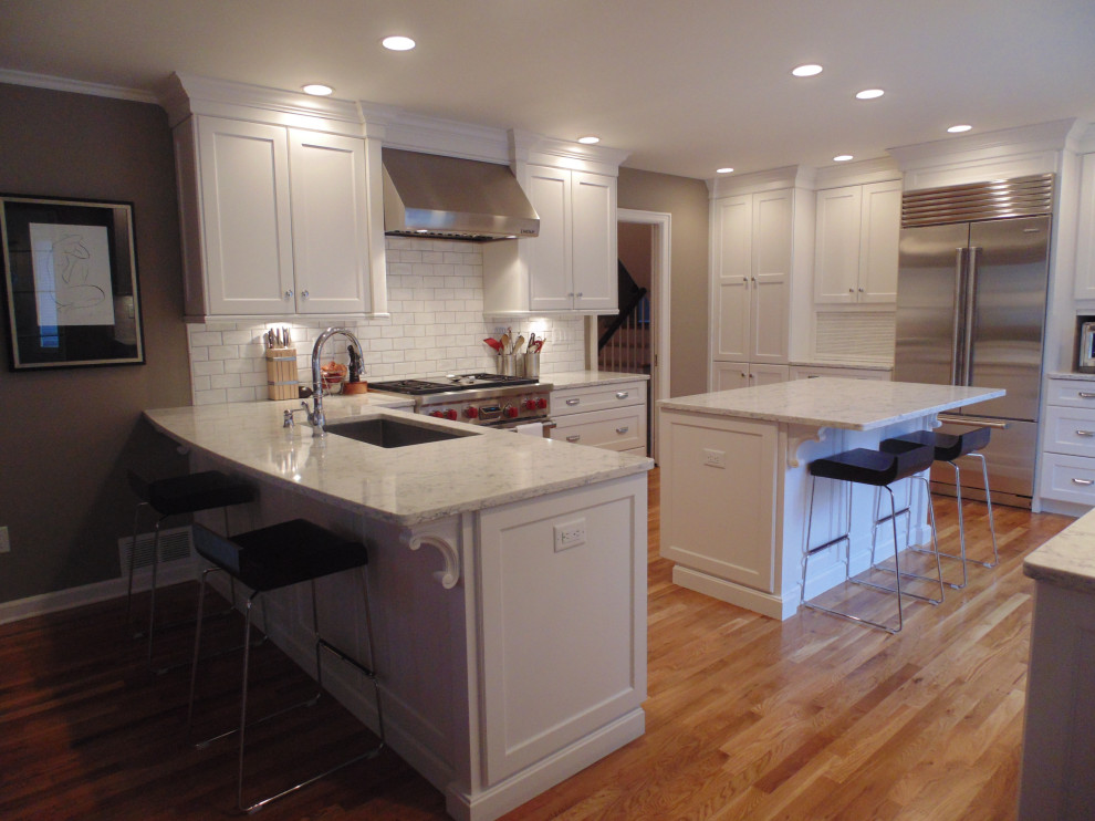 Inspiration for a large transitional u-shaped medium tone wood floor and brown floor eat-in kitchen remodel with an undermount sink, recessed-panel cabinets, white cabinets, quartz countertops, white backsplash, subway tile backsplash, stainless steel appliances, an island and white countertops