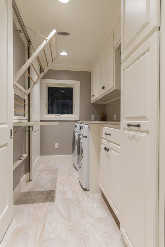 Mid-sized traditional single-wall utility room in Austin with raised-panel cabinets, white cabinets, granite benchtops, beige walls, porcelain floors and a side-by-side washer and dryer.
