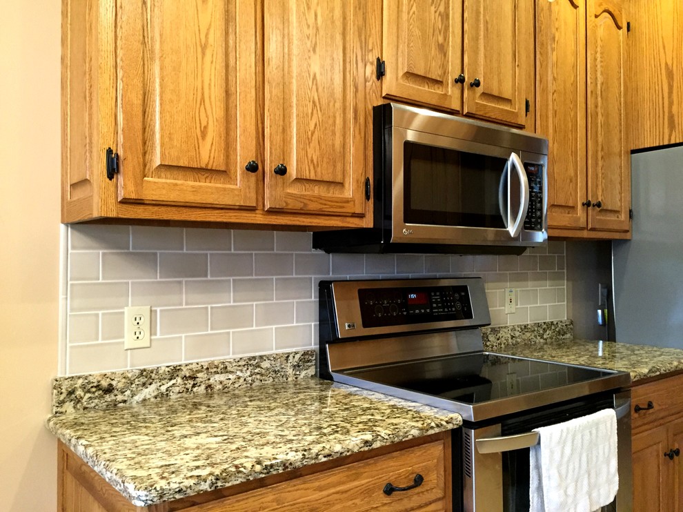 Eat-in kitchen - eat-in kitchen idea in Milwaukee with a double-bowl sink, raised-panel cabinets, medium tone wood cabinets, gray backsplash, subway tile backsplash and stainless steel appliances
