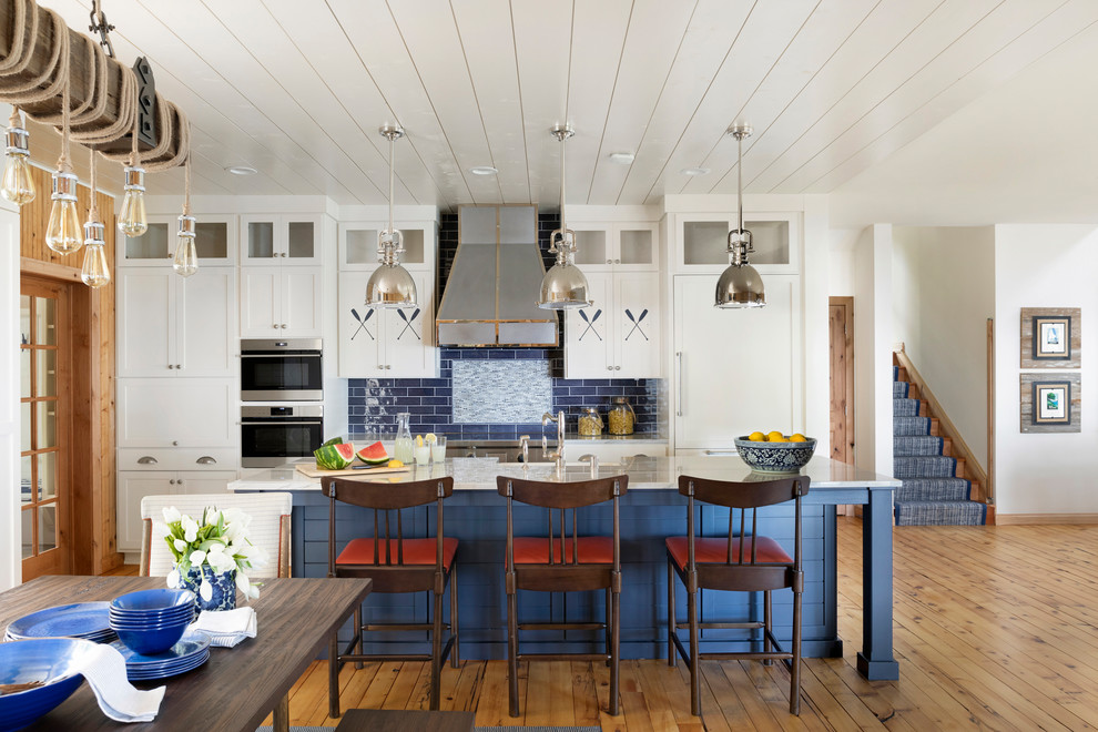 Inspiration for a mid-sized beach style single-wall open plan kitchen in Minneapolis with shaker cabinets, white cabinets, blue splashback, subway tile splashback, stainless steel appliances, medium hardwood floors, with island, white benchtop, a farmhouse sink, granite benchtops and timber.
