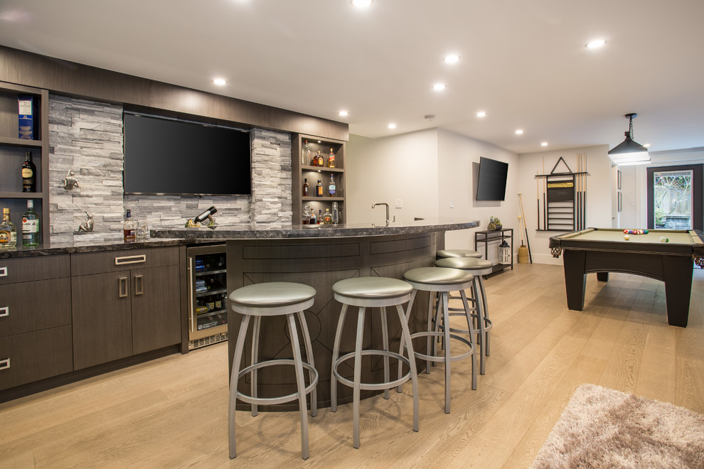 Design ideas for a large transitional u-shaped seated home bar in Vancouver with an undermount sink, brown cabinets, marble benchtops, grey splashback, stone tile splashback, medium hardwood floors, beige floor and black benchtop.