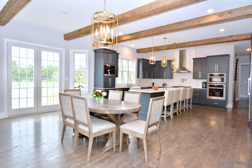 This is an example of a large traditional eat-in kitchen in New York with a farmhouse sink, shaker cabinets, blue cabinets, quartz benchtops, white splashback, ceramic splashback, stainless steel appliances, dark hardwood floors, with island, brown floor and grey benchtop.
