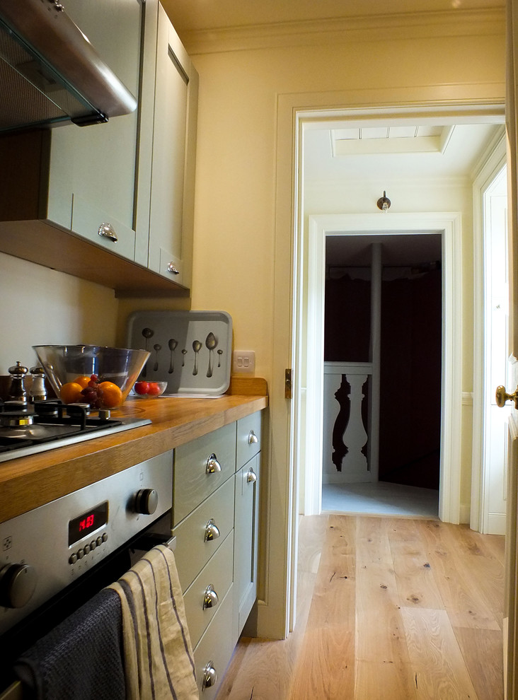 This is an example of a small traditional separate kitchen in Edinburgh with recessed-panel cabinets, green cabinets, wood benchtops, stainless steel appliances and medium hardwood floors.