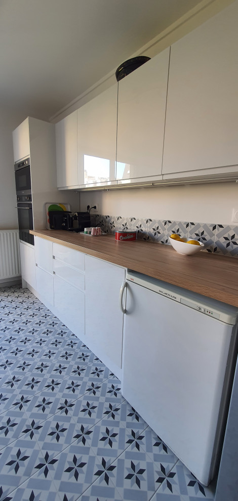 Mid-sized scandinavian galley separate kitchen in Paris with a drop-in sink, beaded inset cabinets, white cabinets, wood benchtops, grey splashback, cement tile splashback, cement tiles, grey floor and brown benchtop.