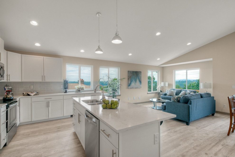 This is an example of a mid-sized contemporary l-shaped eat-in kitchen in Seattle with a double-bowl sink, shaker cabinets, white cabinets, quartzite benchtops, white splashback, subway tile splashback, stainless steel appliances, light hardwood floors, with island and grey floor.