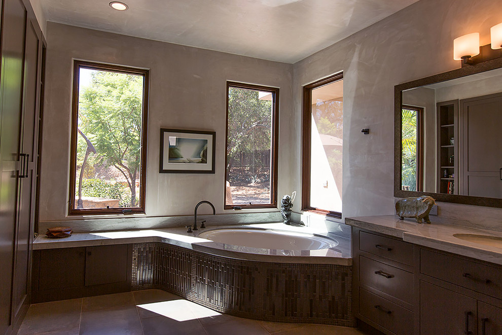 Photo of a mid-sized contemporary master bathroom in Phoenix with a drop-in sink, flat-panel cabinets, dark wood cabinets, granite benchtops, a corner tub, an open shower, a two-piece toilet, gray tile, metal tile, grey walls and porcelain floors.