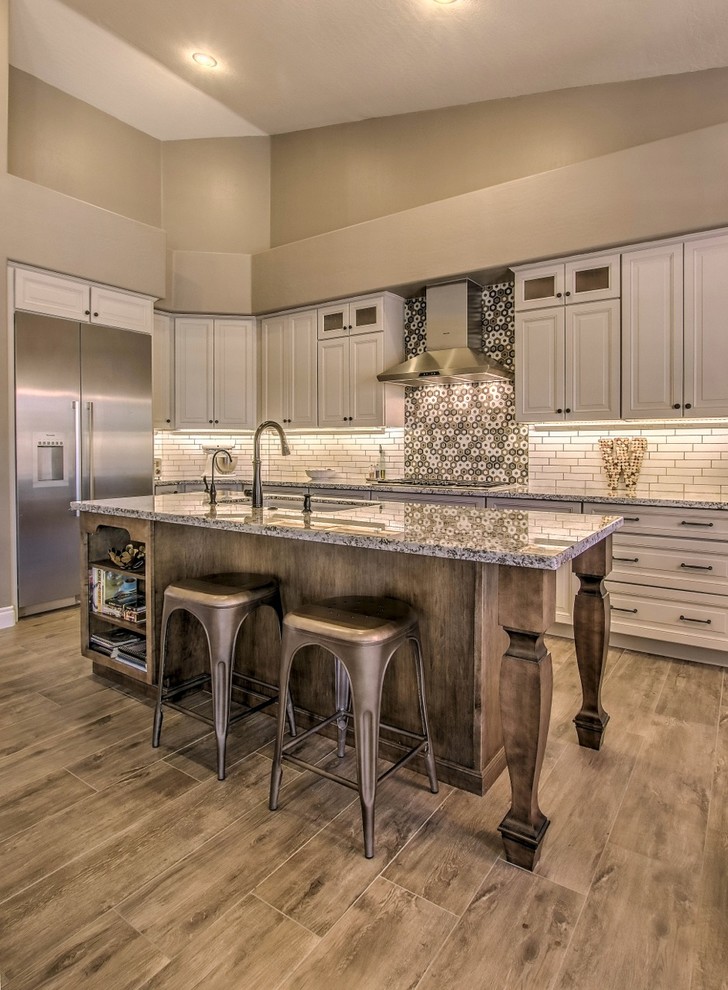 Inspiration for a mid-sized eclectic porcelain tile and brown floor eat-in kitchen remodel in Phoenix with an undermount sink, raised-panel cabinets, white cabinets, granite countertops, white backsplash, ceramic backsplash, stainless steel appliances, an island and white countertops