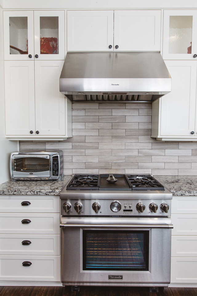 This is an example of a large country u-shaped eat-in kitchen in Boston with a farmhouse sink, white cabinets, granite benchtops, stainless steel appliances, dark hardwood floors, with island, shaker cabinets, brown splashback and matchstick tile splashback.