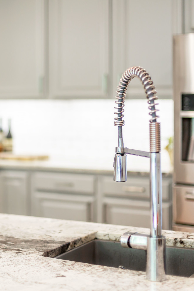 Inspiration for a mid-sized transitional l-shaped medium tone wood floor eat-in kitchen remodel in Richmond with a farmhouse sink, gray cabinets, granite countertops, white backsplash, ceramic backsplash, stainless steel appliances, an island and white countertops
