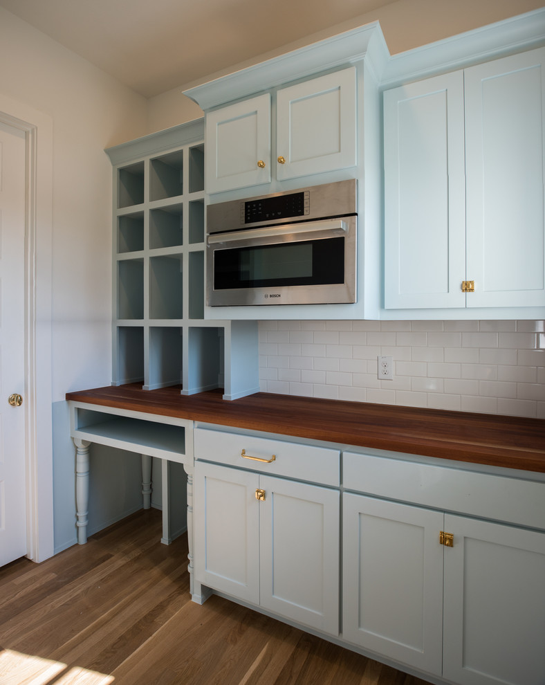 Example of a large transitional u-shaped medium tone wood floor and gray floor kitchen pantry design in Dallas with recessed-panel cabinets, blue cabinets, wood countertops, white backsplash, ceramic backsplash, stainless steel appliances, an island and brown countertops