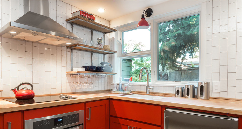 Small contemporary l-shaped open plan kitchen in Portland with an undermount sink, flat-panel cabinets, red cabinets, wood benchtops, white splashback, ceramic splashback, stainless steel appliances, concrete floors and with island.