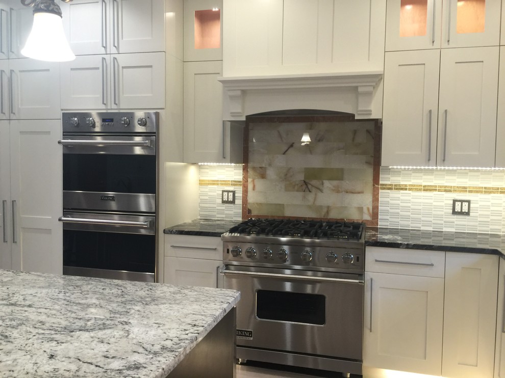 Eat-in kitchen - mid-sized transitional u-shaped light wood floor and beige floor eat-in kitchen idea in Boston with recessed-panel cabinets, white cabinets, stainless steel appliances, a farmhouse sink, granite countertops, beige backsplash, stone tile backsplash, an island and multicolored countertops