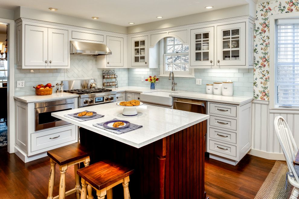 Photo of a country eat-in kitchen in Denver with a farmhouse sink, glass-front cabinets, white cabinets, solid surface benchtops, white splashback, subway tile splashback, stainless steel appliances, medium hardwood floors, with island and white benchtop.