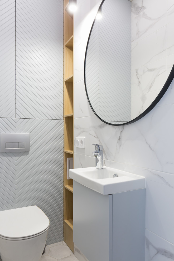 This is an example of a scandinavian powder room in Other with flat-panel cabinets, grey cabinets, a two-piece toilet, white tile, a drop-in sink and white floor.