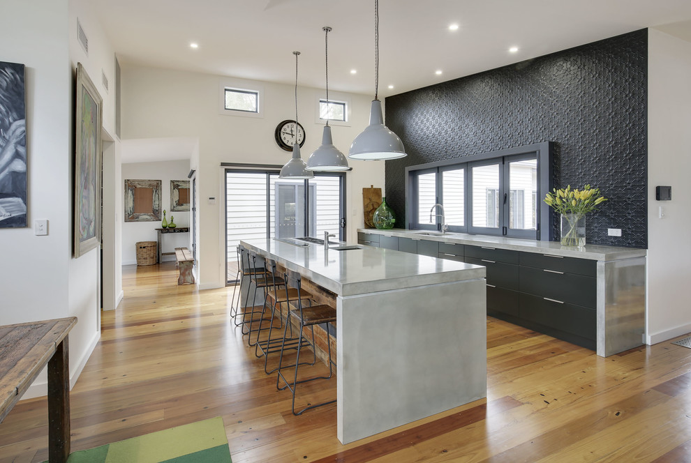 Photo of a mid-sized contemporary single-wall open plan kitchen in Sydney with an undermount sink, flat-panel cabinets, black cabinets, concrete benchtops, black splashback, metal splashback, stainless steel appliances, medium hardwood floors and with island.