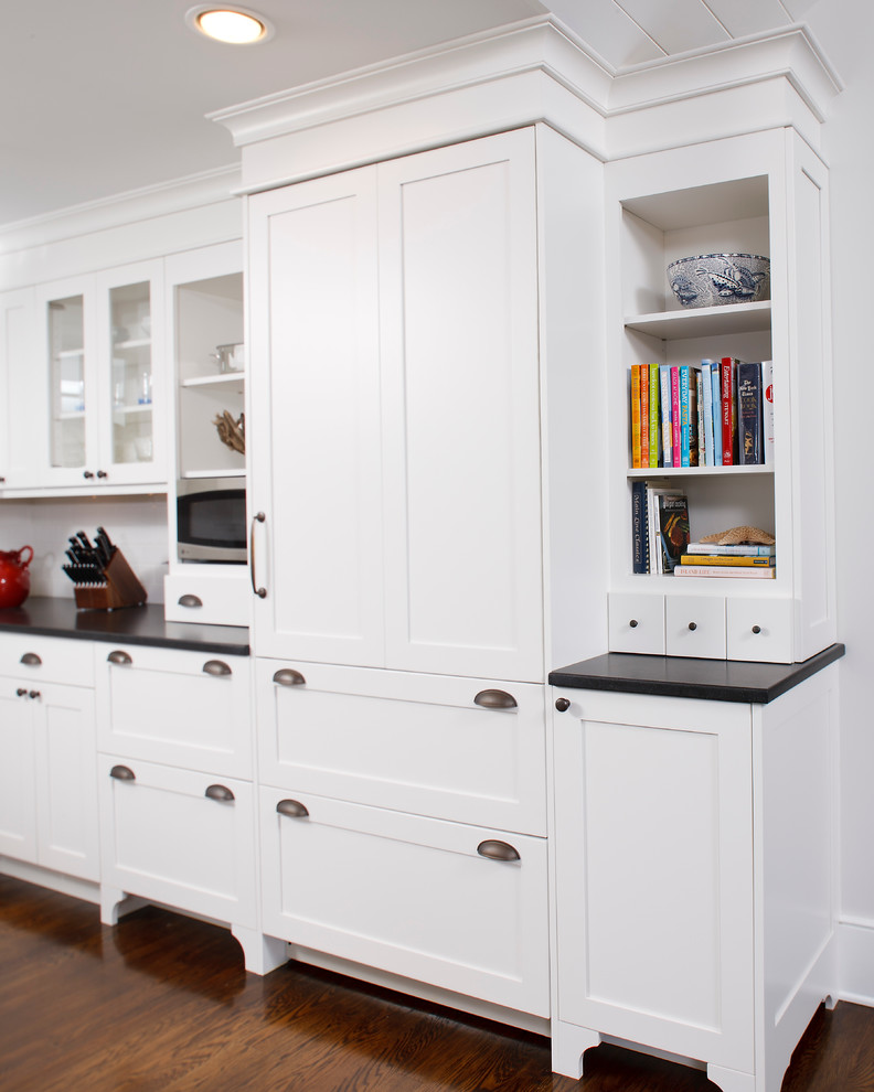 Traditional l-shaped eat-in kitchen in Other with a farmhouse sink, recessed-panel cabinets, white cabinets, granite benchtops, white splashback, subway tile splashback and stainless steel appliances.