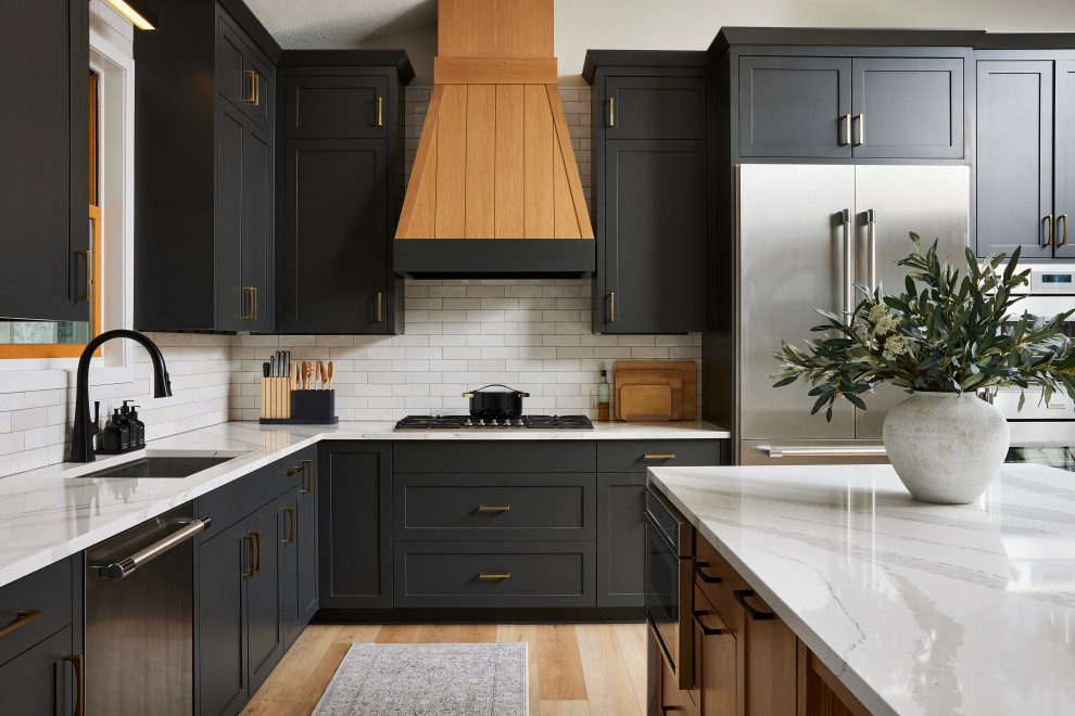Example of a large transitional l-shaped vinyl floor and brown floor eat-in kitchen design in Minneapolis with an undermount sink, shaker cabinets, black cabinets, quartz countertops, white backsplash, porcelain backsplash, stainless steel appliances, an island and white countertops