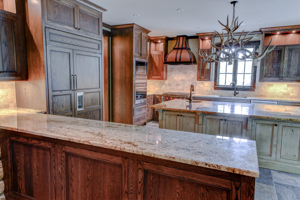 Example of a large mountain style l-shaped slate floor and gray floor enclosed kitchen design with an undermount sink, recessed-panel cabinets, dark wood cabinets, granite countertops, beige backsplash, stone tile backsplash, paneled appliances, a peninsula and brown countertops