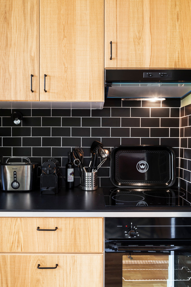 Photo of a small contemporary l-shaped eat-in kitchen in Paris with a single-bowl sink, beaded inset cabinets, light wood cabinets, laminate benchtops, black splashback, subway tile splashback, black appliances, terra-cotta floors and no island.