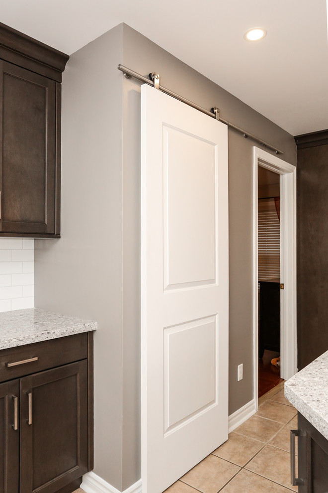 Enclosed kitchen - mid-sized transitional u-shaped enclosed kitchen idea in Toronto with an undermount sink, recessed-panel cabinets, dark wood cabinets, quartz countertops, white backsplash, porcelain backsplash, stainless steel appliances and an island