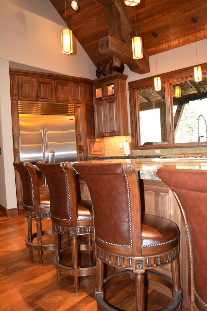 Example of a mid-sized mountain style l-shaped medium tone wood floor open concept kitchen design with raised-panel cabinets, medium tone wood cabinets, granite countertops, beige backsplash, ceramic backsplash, stainless steel appliances and an island