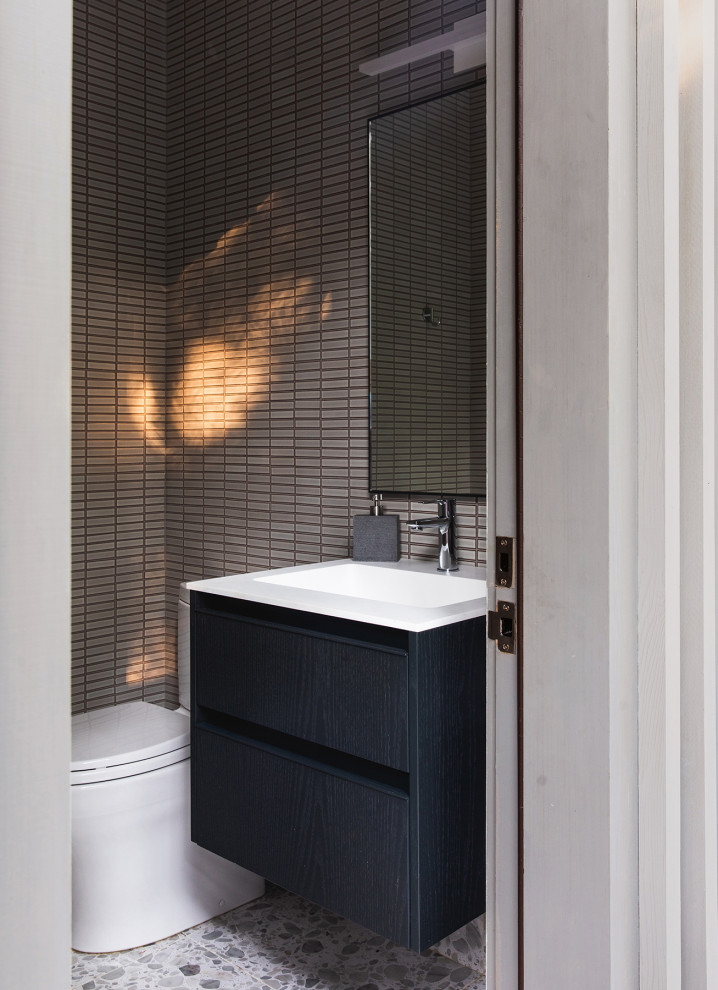 Inspiration for a small contemporary cloakroom in New York with flat-panel cabinets, black cabinets, a one-piece toilet, grey tiles, stone slabs, grey walls, terrazzo flooring, a built-in sink, engineered stone worktops, grey floors, white worktops and a floating vanity unit.