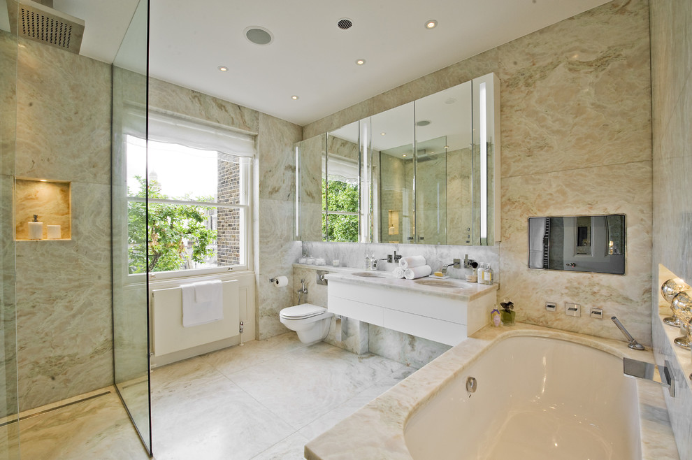 This is an example of a transitional master bathroom in London with a wall-mount sink, marble benchtops, a wall-mount toilet, marble floors, flat-panel cabinets, white cabinets and an undermount tub.