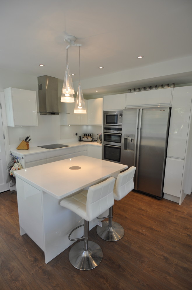 This is an example of a mid-sized modern u-shaped open plan kitchen in London with an undermount sink, flat-panel cabinets, white cabinets, quartzite benchtops, white splashback, stainless steel appliances, dark hardwood floors and with island.