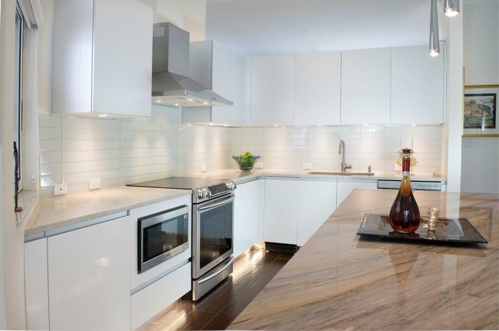 Inspiration for a mid-sized contemporary l-shaped eat-in kitchen in Miami with an integrated sink, flat-panel cabinets, white cabinets, granite benchtops, white splashback, stainless steel appliances, porcelain floors, with island, subway tile splashback and brown floor.