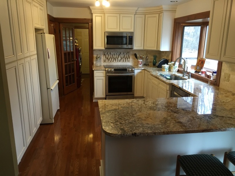 Example of a mid-sized transitional u-shaped medium tone wood floor eat-in kitchen design with an undermount sink, flat-panel cabinets, white cabinets, granite countertops, beige backsplash, stone tile backsplash, stainless steel appliances and a peninsula