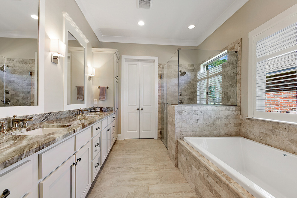 This is an example of a large transitional master bathroom in New Orleans with beaded inset cabinets, white cabinets, a freestanding tub, a corner shower, beige tile, stone tile, beige walls, porcelain floors, an undermount sink, granite benchtops, beige floor and a hinged shower door.