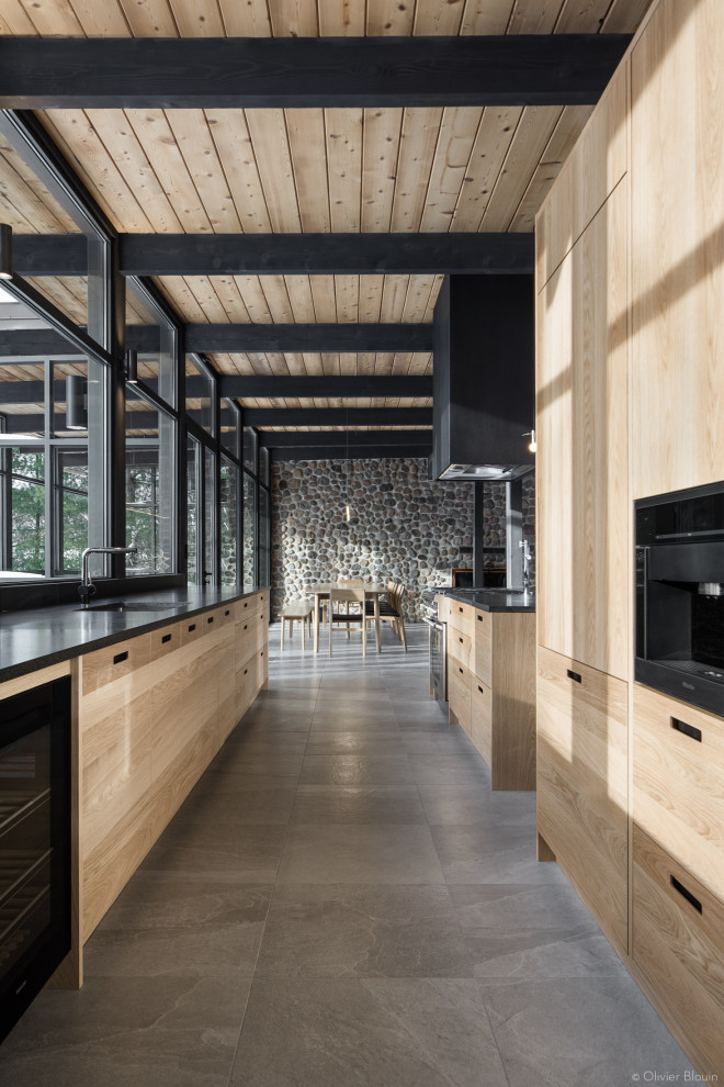 Design ideas for a large modern galley kitchen in Montreal with an undermount sink, flat-panel cabinets, light wood cabinets, granite benchtops, panelled appliances, ceramic floors, grey floor, black benchtop and timber.
