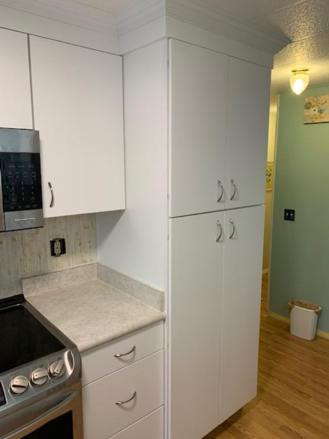 Kitchen pantry - large u-shaped kitchen pantry idea with a farmhouse sink, flat-panel cabinets, white cabinets, laminate countertops, white backsplash, stainless steel appliances, a peninsula and white countertops