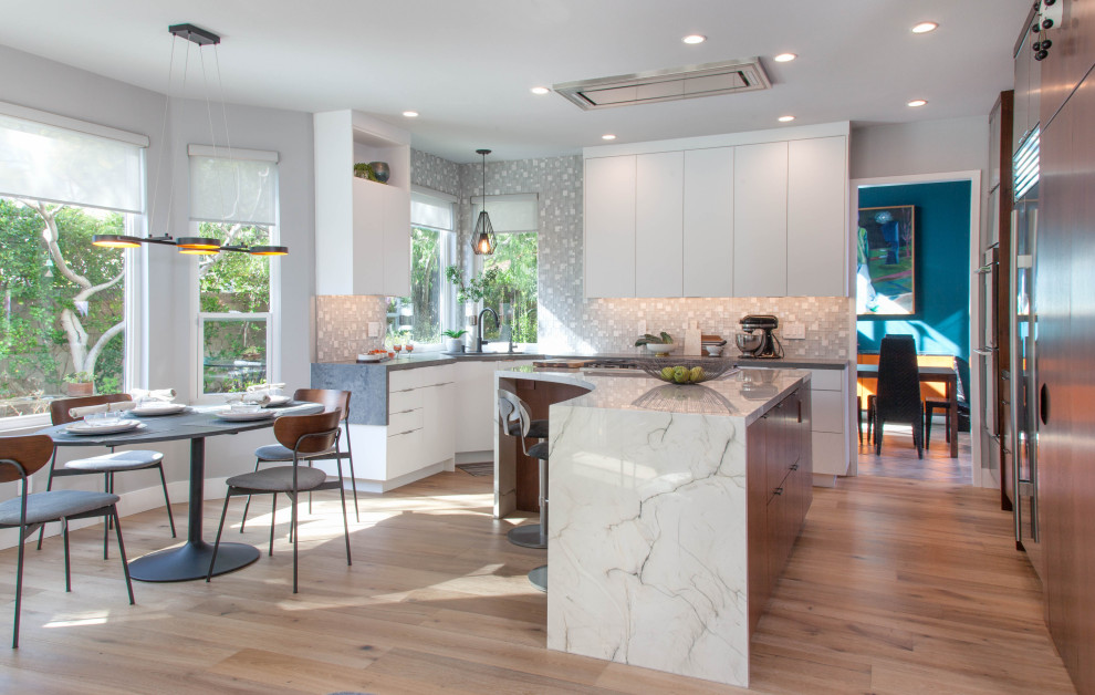 Photo of a mid-sized contemporary l-shaped kitchen in Denver with an undermount sink, flat-panel cabinets, white cabinets, quartzite benchtops, stainless steel appliances, medium hardwood floors, with island, beige floor, grey splashback and grey benchtop.