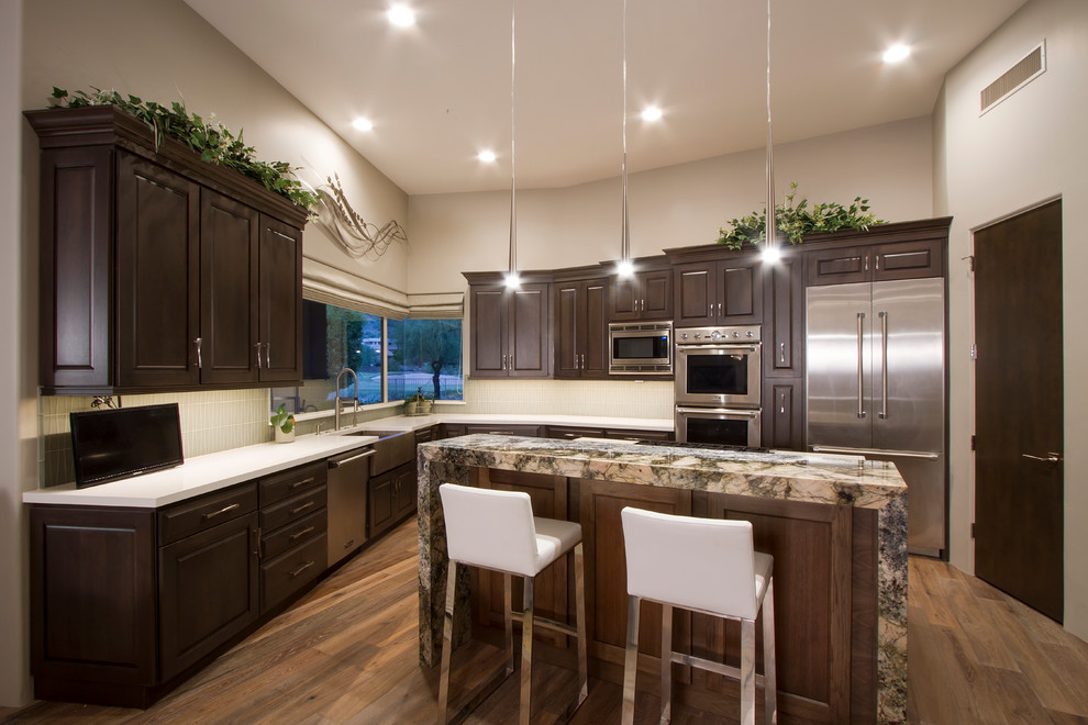 Mid-sized transitional l-shaped light wood floor and brown floor eat-in kitchen photo in Phoenix with a farmhouse sink, shaker cabinets, quartzite countertops, glass sheet backsplash, stainless steel appliances, an island, dark wood cabinets, beige backsplash and white countertops