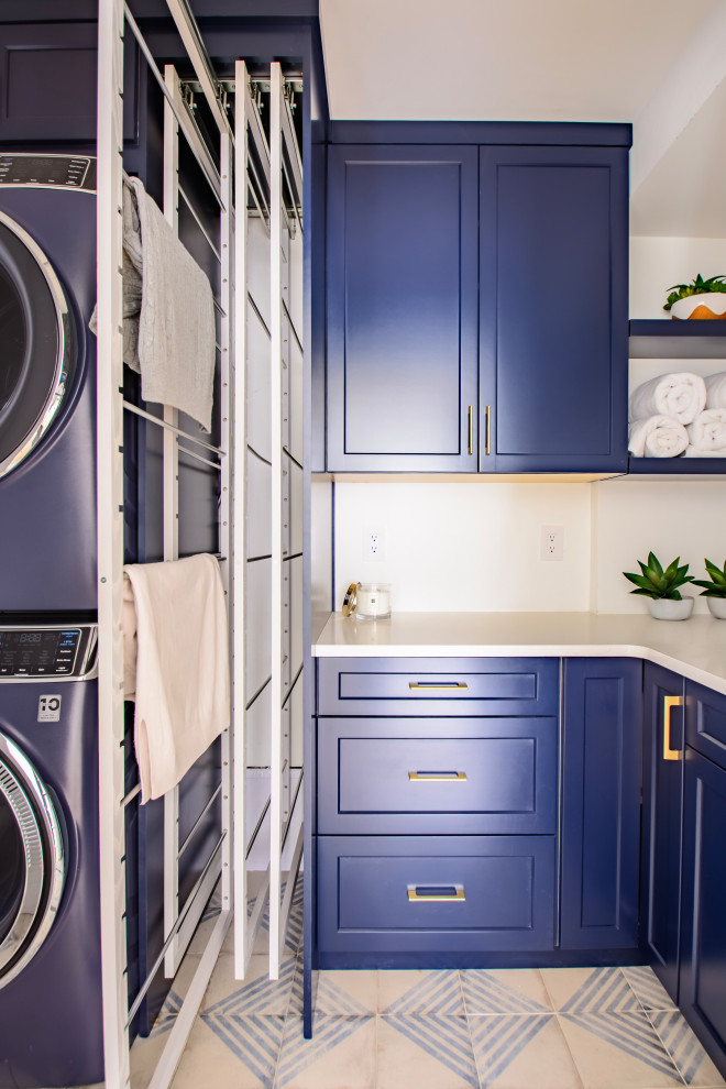 Mid-sized modern l-shaped dedicated laundry room in Denver with an undermount sink, shaker cabinets, blue cabinets, quartz benchtops, white walls, ceramic floors, a stacked washer and dryer, blue floor and white benchtop.