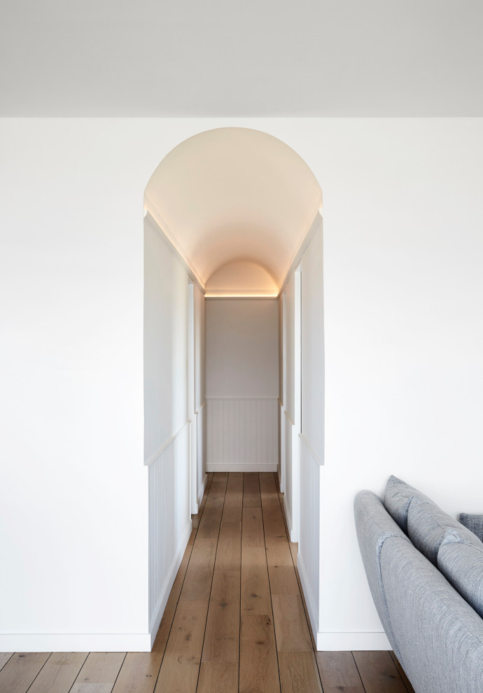 Photo of a small beach style hallway in Sydney with white walls, medium hardwood floors, brown floor and vaulted.