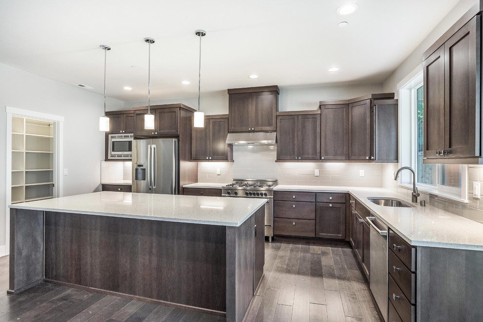 Inspiration for a large traditional u-shaped open plan kitchen in Seattle with an undermount sink, shaker cabinets, brown cabinets, quartz benchtops, grey splashback, subway tile splashback, stainless steel appliances, dark hardwood floors, with island and brown floor.
