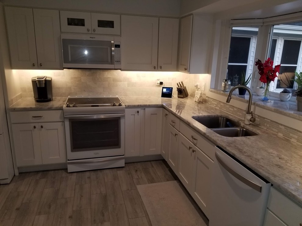 Example of a mid-sized transitional l-shaped laminate floor and white floor eat-in kitchen design in Chicago with a double-bowl sink, shaker cabinets, white cabinets, quartzite countertops, white backsplash, subway tile backsplash, white appliances, no island and white countertops