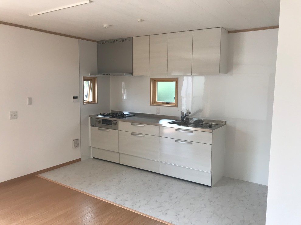 This is an example of a small single-wall open plan kitchen in Tokyo Suburbs with a single-bowl sink, flat-panel cabinets, white cabinets, stainless steel benchtops, glass sheet splashback, light hardwood floors, no island and white floor.