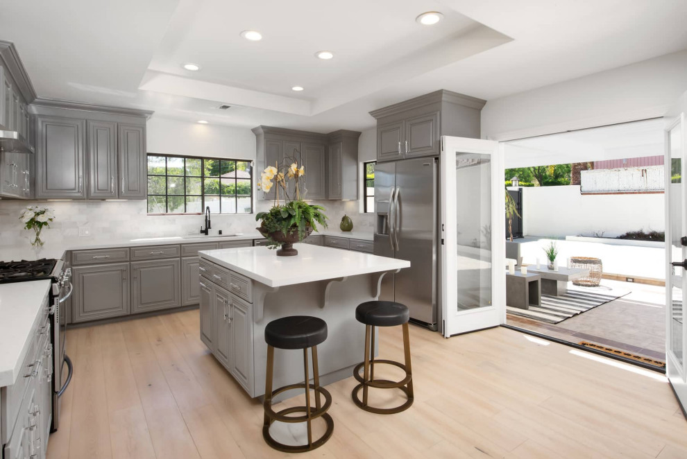 Large midcentury u-shaped eat-in kitchen in Los Angeles with an undermount sink, raised-panel cabinets, grey cabinets, marble benchtops, white splashback, marble splashback, stainless steel appliances, light hardwood floors, with island, white benchtop and recessed.