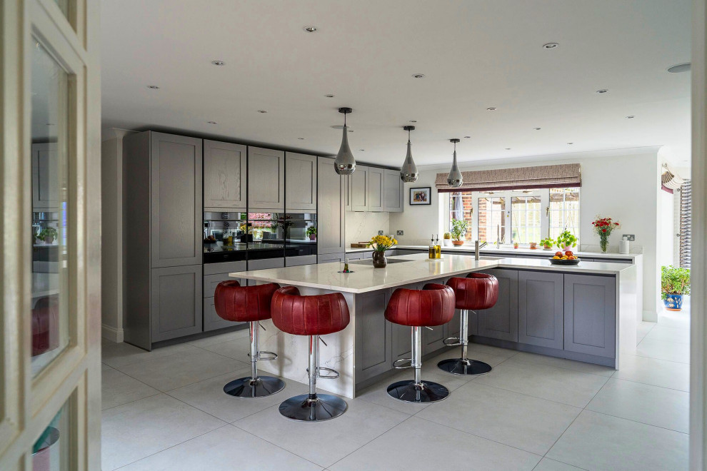 This is an example of a medium sized classic l-shaped open plan kitchen in Oxfordshire with a single-bowl sink, recessed-panel cabinets, grey cabinets, marble worktops, black appliances, an island, grey floors and white worktops.