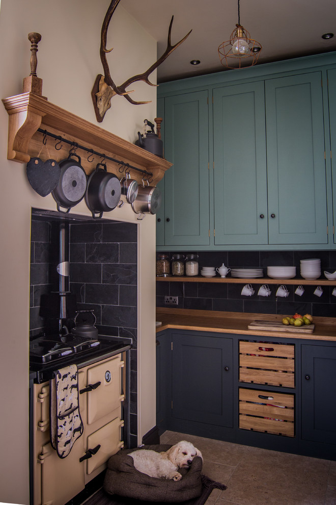 This is an example of a small traditional l-shaped eat-in kitchen in Gloucestershire with shaker cabinets, wood benchtops, black splashback, stone tile splashback, coloured appliances, limestone floors, a drop-in sink, green cabinets and no island.