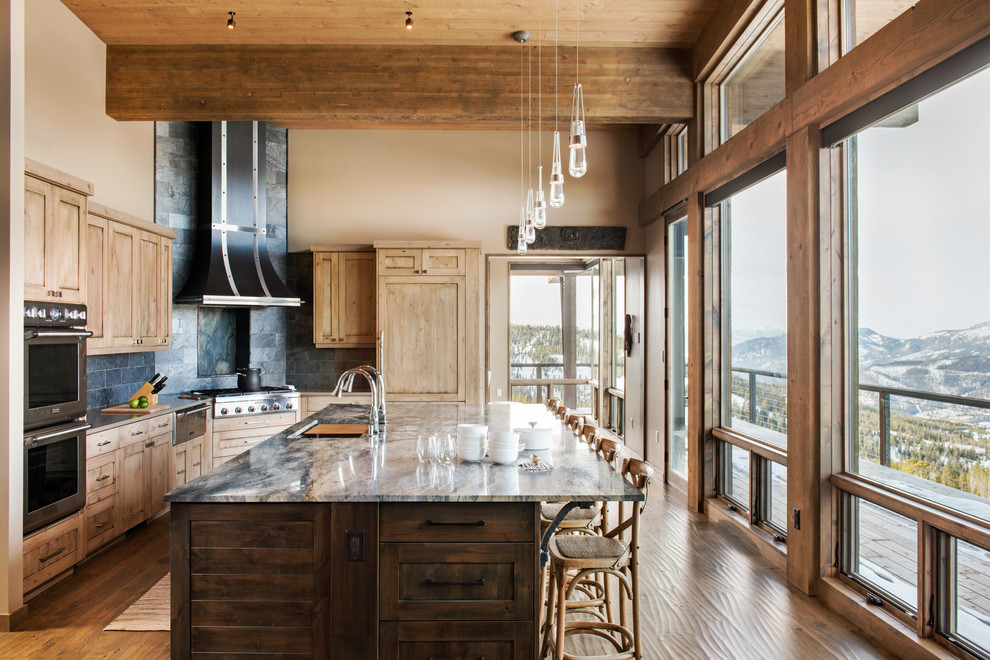 Example of a mountain style l-shaped medium tone wood floor and brown floor kitchen design with an undermount sink, shaker cabinets, medium tone wood cabinets, gray backsplash, paneled appliances and an island