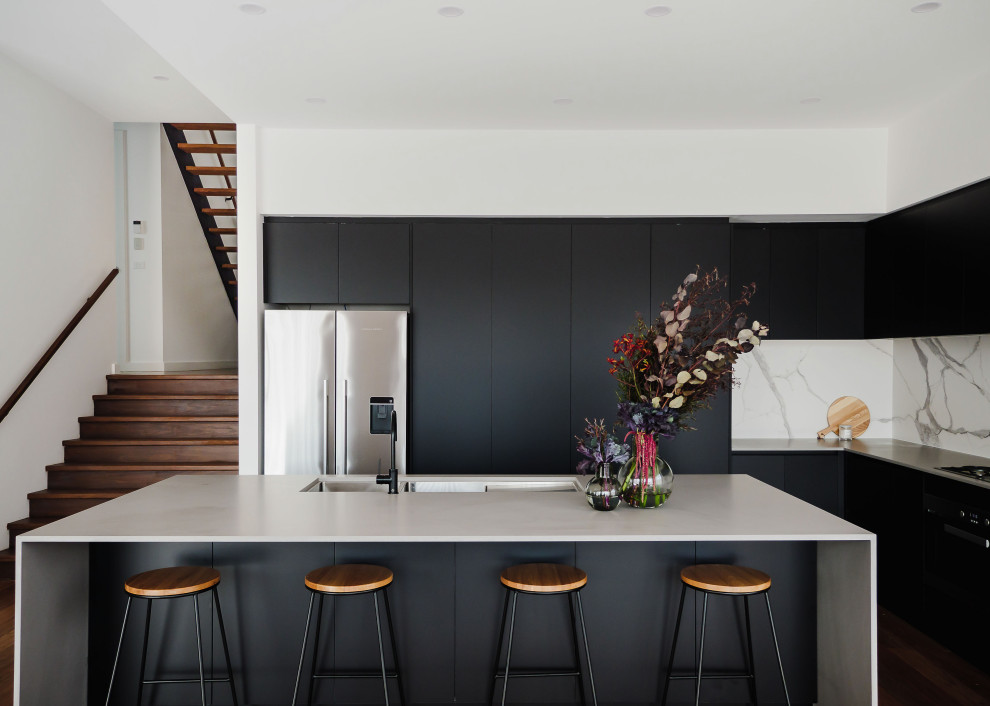 Inspiration for a contemporary l-shaped kitchen in Melbourne with a triple-bowl sink, flat-panel cabinets, black cabinets, multi-coloured splashback, stone slab splashback, stainless steel appliances, dark hardwood floors, with island, brown floor and grey benchtop.